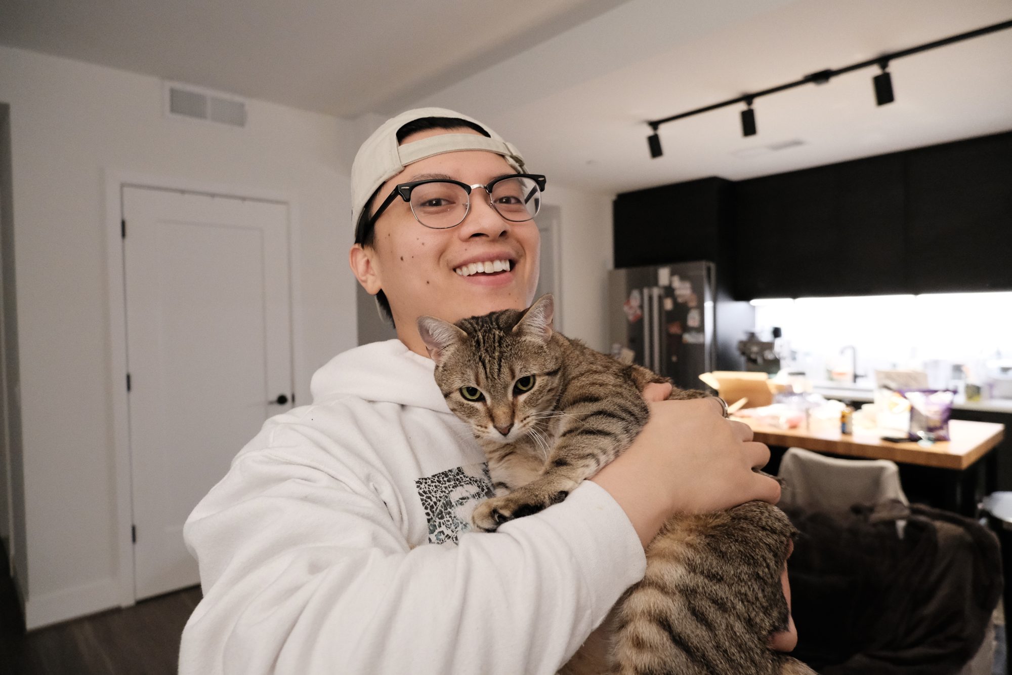 Raymond smiling while holding his tabby cat at home